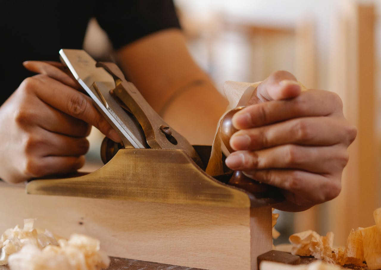 Crop unrecognizable male master smoothing surface of wooden plank using jack plane in workshop